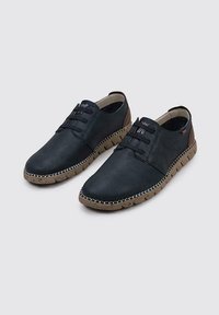 Zapatos de cuero negro con un acabado texturizado, que cuentan con un diseño sin cordones, bandas elásticas y un acento de tacón marrón. Detalles de costura y suela resistente.