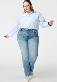 Lichtblauw gestreept overhemd met knopen en lange mouwen, gecombineerd met vervaagde blauwe jeans met rechte pijpen en witte instapschoenen met polkadots.