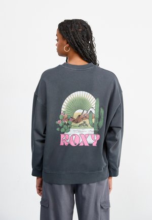 Dark gray sweatshirt with a relaxed fit, featuring a colorful desert scene graphic and the word "ROXY" in pink at the back.