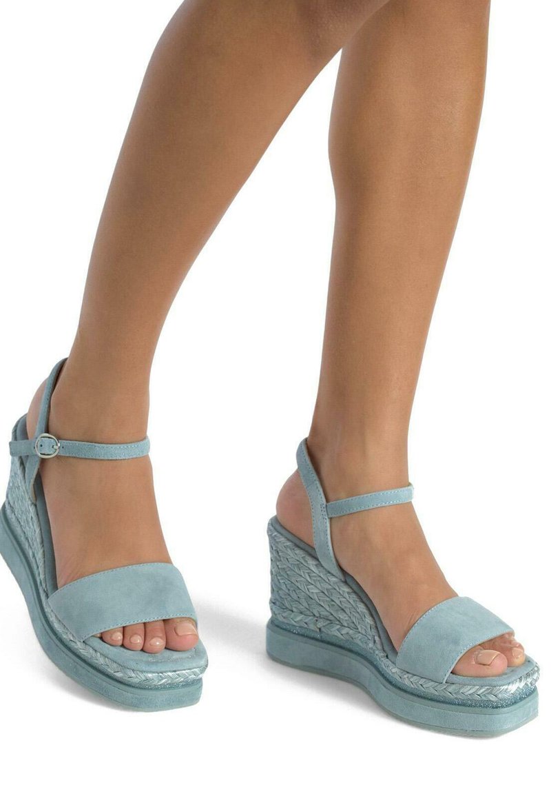 Sandali con zeppa in suede azzurro chiaro, con una fascia larga sopra le dita dei piedi e cinghietta alla caviglia, con una texture intrecciata sulla zeppa per un maggior dettaglio.