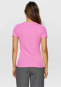 Różowa koszulka z krótkim rękawem wykonana z bawełny, z okrągłym dekoltem i dopasowanym krojem, w połączeniu z szarymi spodniami w prążki.