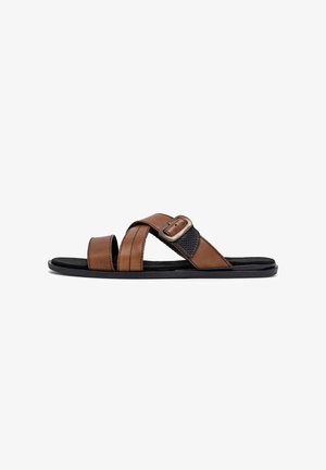 Pruunid nahast liugstüüpi sandaalid, millel on ristkinnitusega rihmad, tekstuuriga must rõhutus ja külgmine pandlaga kinnitus. Tasapinnaline tald, sileda viimistlusega.