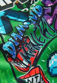 Kolorowy nadruk na tkaninie z tekstem w stylu graffiti "DIAMOND NEW YORK" w niebieskim, czarnym i białym na zielonym i czerwonym tle.