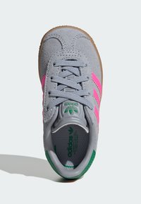 Pilkas zomšinis sportinis batelis su rožinėmis juostelėmis, žaliais akcentais ir baltu logotipu, turintis tekstūruotą vidpadį ir raištelių užsegimą.