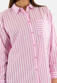 Camicia leggera con bottoni, caratterizzata da un motivo a righe verticali rosa e bianche, una tasca sul petto e colletto appuntito.