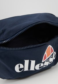 Pochette in tessuto blu navy con chiusura a zip, dotata di logo bianco e dettaglio arancione. L'interno presenta una fodera in tessuto nero semplice.