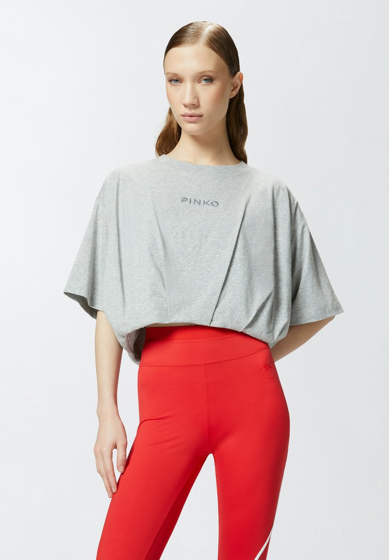 T-shirt grigia a maniche corte con taglio corto, caratterizzata dal logo "PINKO." Abbinata a leggings rossi a vita alta. Tessuto morbido con una vestibilità comoda.