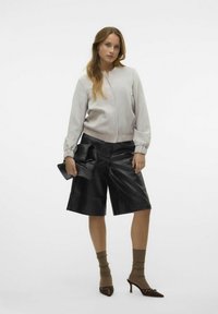 Ljusgrå bomberjacka, svarta läderbyxor med vida ben, svart puffig klutch, bruna strumpor och spetsiga skor med dekorativa detaljer.