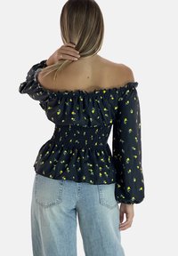 Off-shoulder sort bluse med gult blomstermønster, smocket talje og lange ærmer. Krydret med højtaljede denimjeans.