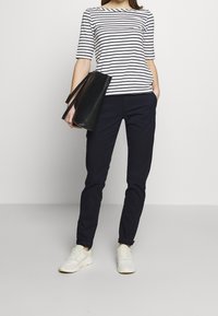 Pruhovaná námořnická modrá a bílá košile s tříčtvrtečními rukávy, zkombinovaná s námořnickými kalhotami. Nese černou kabelku a má na sob ě světlé tenisky.