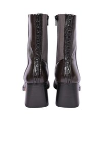 Bottines noires à finition brillante, dotées d'une fermeture éclair à l'arrière et de panneaux latéraux texturés. Le talon bloc apporte stabilité et hauteur.
