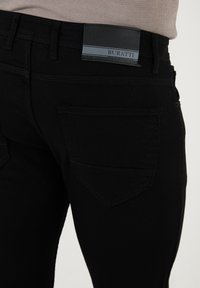 Svarta denimjeans med smal passform, med tvåfickorsdesign och subtila sömmar. Etiketten säger "Buratti." Slät textur.