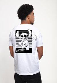 Camiseta de algodón blanca con un gráfico negro de un personaje de dibujos animados en la parte posterior, sobre un fondo de rayas horizontales, con texto en un rectángulo negro.
