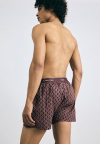 Bordo bokseri ar ģeometrisku rakstu, elastīgu jostu ar "Calvin Klein" zīmolu un mīkstu auduma tekstūru.