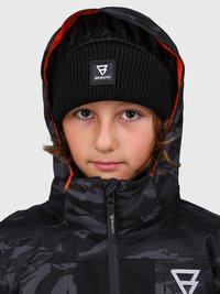 Junge Person, die eine schwarze Strickmütze und eine schwarze gemusterte Kapuzenjacke mit orangefarbiger Innenausstattung sowie Brunotti-Logos auf beiden Kleidungsstücken trägt.