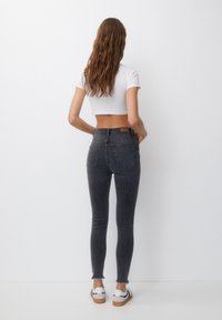 Szare, wysoka talia dżinsy skinny z postrzępionymi krawędziami, w połączeniu z białą, krótką koszulą i białymi trampkami. Widok z tyłu, pokazujący kieszenie.