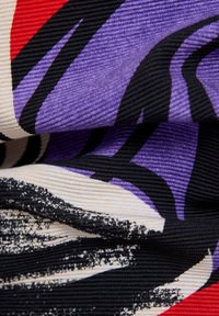 Multicolored fabric pattern featuring purple, black, red, and cream. Distinctive ribbed texture with abstract design elements.