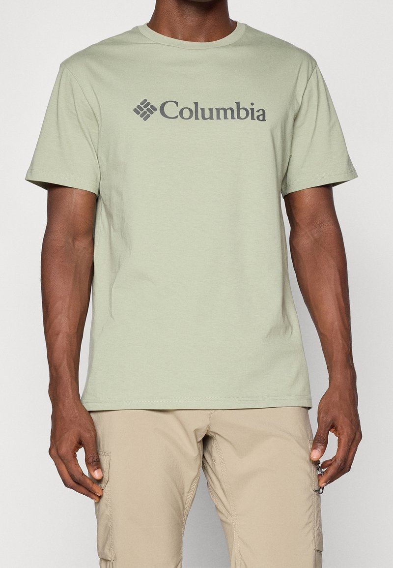 Svetle zelené bavlněné tričko s logem "Columbia" v tmavě šedé barvě, kulatý výstřih a krátké rukávy. Kombinováno se světle béžovými cargo šortkami.
