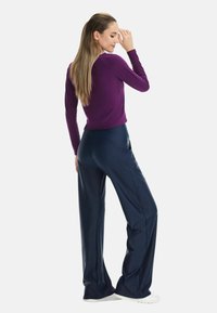 Lila Langarmshirt kombiniert mit marineblauen Hosen mit weitem Bein, mit glatter Textur und moderner Silhouette. Weiße Schuhe komplettieren das Outfit.