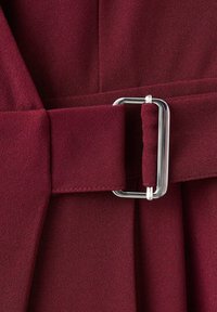 Hnědý páskový oděv z texturované látky, s obdélníkovou stříbrnou kovovou přezkou a pečlivým šitím na pásu a skladech.