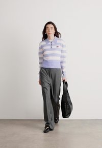 Pulover striped mov și alb cu guler și nasturi, asociat cu pantaloni largi gri și o geantă tote neagră.