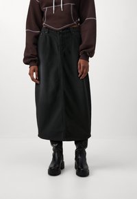 Falda maxi de mezclilla negra con detalle de costura frontal, cintura alta y cinturilla elástica, combinada con botas de cuero negras hasta el tobillo.