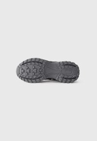 Suola di scarpa sportiva nera con un motivo di battistrada profondo, materiale in gomma, superficie texturizzata e dettagli in rilievo per presa e trazione.