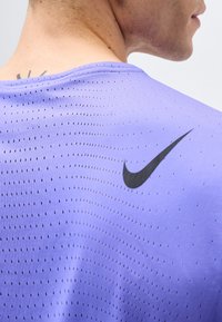 Close-up of upper back and neck wearing a light purple perforated sports shirt with a black Nike swoosh logo.
