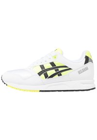 Scarpe sportive bianche con dettagli neri e neon gialli. Presentano una tomaia in pelle liscia, una suola ammortizzata e pannelli in rete testurizzata.