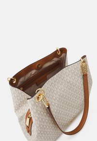 Beige handtas met patroon, met een bruine leren binnenkant, gouden hardware en een schouderriem. Voorzien van een ritsvak en een magnetische drukknoopsluiting.