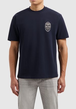 Marineblauwe korte mouwen t-shirt van katoen, met een klein wit grafisch patch op de linkerborst en een ontspannen pasvorm.