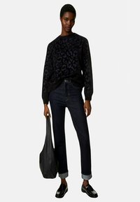 Maglione nero con motivo leopardo sottile, jeans a gamba dritta blu scuro, risvoltati, mocassini neri e borsa tote nera.