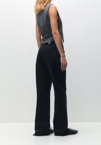 Grau ärmelloses Oberteil mit einer taillierten Silhouette und Rückenknotendetail, kombiniert mit hoch taillierten, schwarzen weit geschnittenen Jeans und schwarzen Slippers.