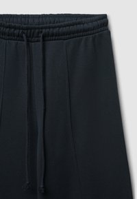 Un pantalon de survêtement noir présente une taille élastique avec des cordons de serrage réglables, une texture de tissu lisse et des détails de couture latéraux.