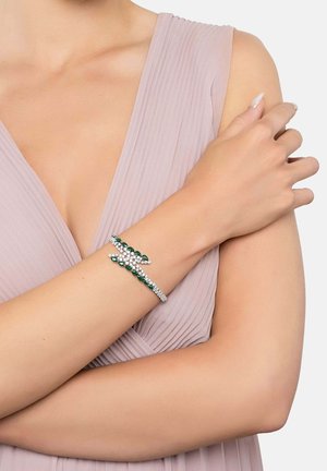 Silver cuff bracelet featuring green and clear gemstones, with a leaf-shaped design. Smooth metal surface with sparkle from the stones.