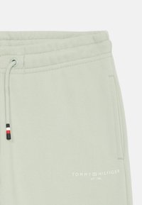 Ljusgröna träningsoverallsbyxor med dragsko i midjan, med en subtil textur och "Tommy Hilfiger"-logotypen i vitt i nedre vänstra hörnet.
