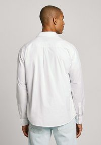 Camicia bianca a maniche lunghe con colletto classico, polsini abbottonati e taglio dritto. Tessuto morbido, senza motivi visibili.
