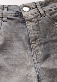 Metallisk grå denimtyg med en framknapp och dragkedjestängning, bälteshällor och subtila texturvariationer.