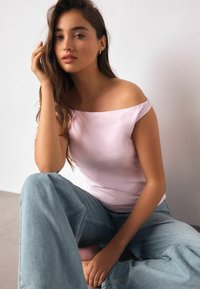 Hele roosa õlgadeta pluus, mis on kombineeritud lahtiste helesiniste teksadega. Kangas paistab sile ja veidi läikiv.