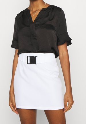 Vrouw draagt een zwarte blouse met korte mouwen, ingestopt in een witte minirok met een brede riem en zwarte gesp.
