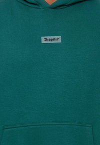 Haut à capuche vert en tissu doux, avec une poche avant, un cordon de serrage et un patch logo rectangulaire portant l'inscription "Dropsize".