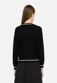 Maglione nero a maglia con scollatura tonda, maniche lunghe e accenti a strisce bianche sul colletto e sui polsini. Tessuto morbido, vestibilità aderente.