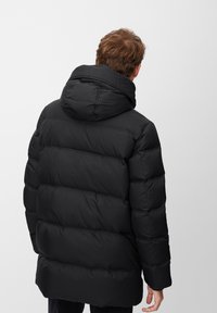 Chaqueta tipo plumas negra con capucha, diseño acolchado y costuras horizontales. El material parece suave y ligero.
