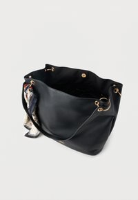 Black leather handbag with gold eyelets and a magnetic snap closure, featuring a patterned silk scarf tied to one handle.