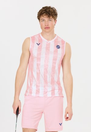 Ung mand iført lyserød og hvidstribet, ærmeløs sportstrøje og lyserøde shorts, der holder en badmintonketcher mod en hvid baggrund.