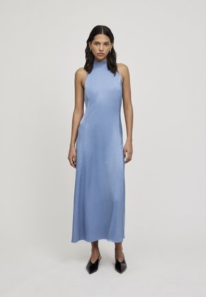 Lichtblauwe, mouwloze maxi-jurk met een hoge halslijn, gladde textuur en vloeiende ontwerp, gecombineerd met zwarte pumps met puntige neuzen.