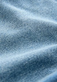Tela de mezclilla azul claro con una superficie suave y texturizada. La trama es visible, mostrando una calidad suave y ligeramente elástica.