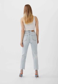 Ljusblå högmidjade jeans med fransar i kanten, med två bakfickor och en tan läderlapp vid midjan. Stylar med en vit linne.