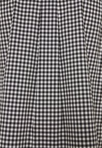 Tessuto gingham bianco e nero con un motivo a quadretti, caratterizzato da una texture plissettata. Il tessuto ha una finitura liscia e un layout a griglia uniforme.