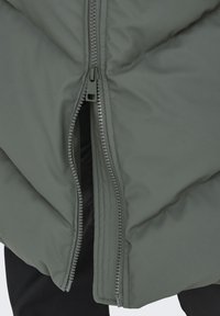 Prim-plan al unei jachete gri căptușite, parțial deschisă, care arată dinții fermoarului și textura țesăturii.